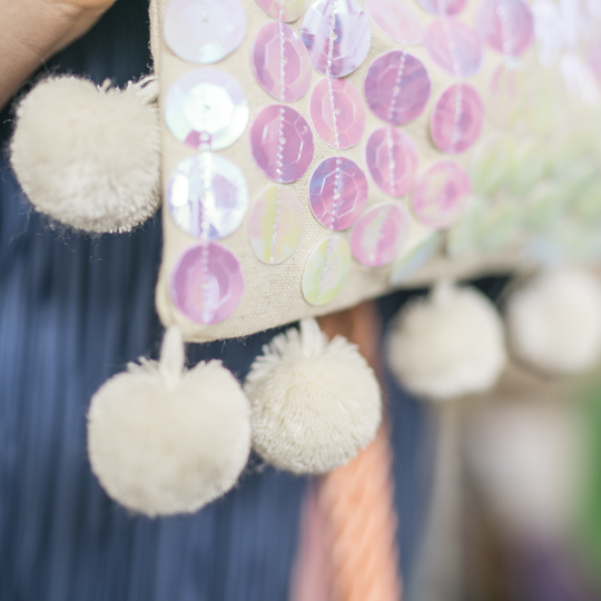 Detailansicht eines textilen Projekts mit schimmernden Pailletten in Pastellfarben und mehreren weissen Pompons am Saum image number