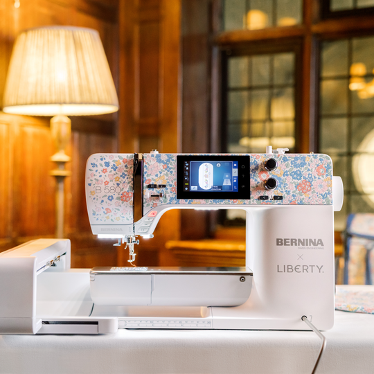 BERNINA 580 Liberty Edition sewing machine with floral design on a quilting table, shown in a warmly lit, wood-paneled sewing room. image number