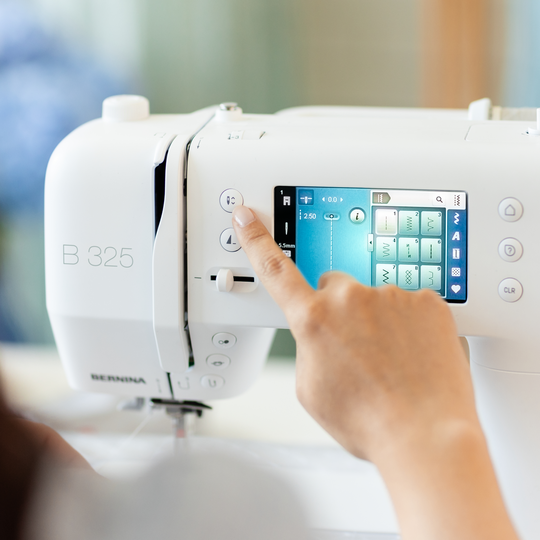 Person selecting a stitch on the touchscreen of the BERNINA B 325 sewing machine in a bright sewing room environment image number