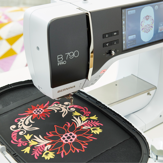 BERNINA 790 PRO Stickmaschine im Einsatz mit eingespanntem schwarzen Stoff, auf den ein bunter floraler Kranz im Stickrahmen gestickt wird image number