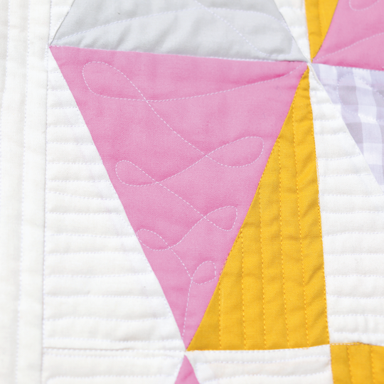 Detailaufnahme eines modernen Quilts mit weissen, rosa und gelben Stoffdreiecken und dekorativen Freihandquiltlinien auf der rosa Fl&auml;che image number