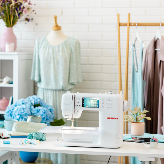 BERNINA B 325 sewing machine on a bright sewing table with fabrics and flowers, set in a modern garment‑sewing studio with dress form. image number