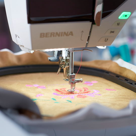 BERNINA Stickmaschine beim Sticken eines bunten Blumenmotivs auf eingespanntem Stoff im Stickrahmen in Nahaufnahme image number