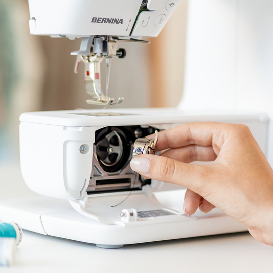 Hand inserting a bobbin case into the front-loading hook system of a BERNINA B 335 sewing machine for precise stitching image number