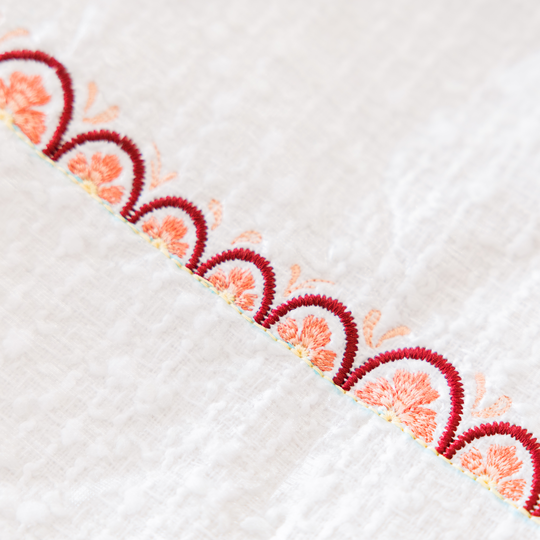 Weisser Stoff mit dekorativer, halbkreisfoermiger Bogenstickerei in Rot und Apricot entlang einer diagonalen Kante image number