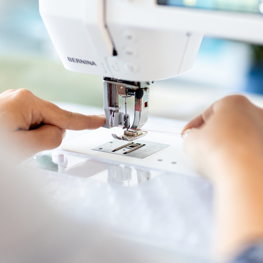 Hands guiding fabric under the presser foot of a BERNINA B 335 sewing machine, focusing on precise needle area for accurate stitching. image number