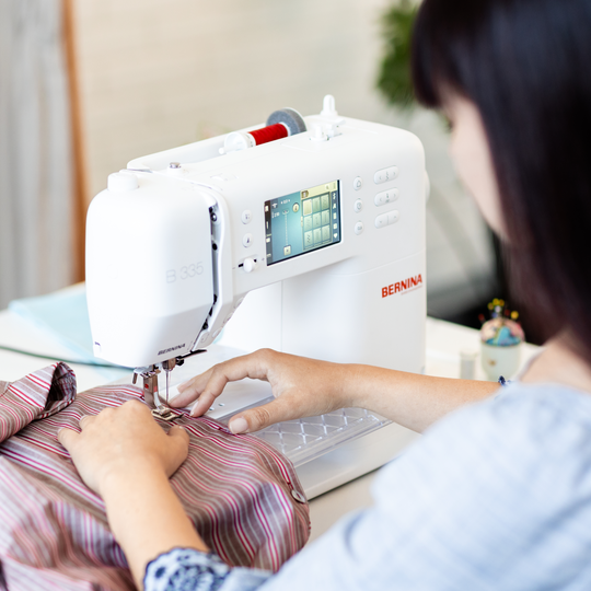 Frau n&auml;ht ein gestreiftes Kleidungsst&uuml;ck mit der weissen BERNINA 335, der Bildschirm der N&auml;hmaschine zeigt farbige Sticheinstellungen image number