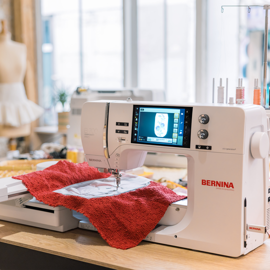 BERNINA 700 PRO Stickmaschine beim Besticken eines roten Quilts im hellen Atelier, mit grossz&uuml;gigem Freiarm und Farbdisplay mit Stickmotiv image number
