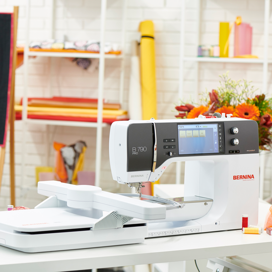 BERNINA 790 PRO Stickmaschine mit angebautem Stickmodul auf einem weissen Tisch in kreativem N&auml;hatelier mit bunten Stoffen und Blumen im Hintergrund image number