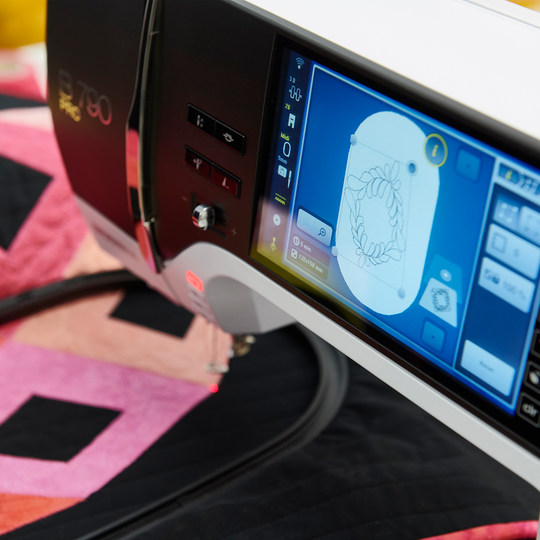 BERNINA 790 PRO Stickmaschine mit beleuchtetem Farb-Touchscreen beim Sticken eines runden Motivs auf einer bunt gepatchten Quiltdecke image number